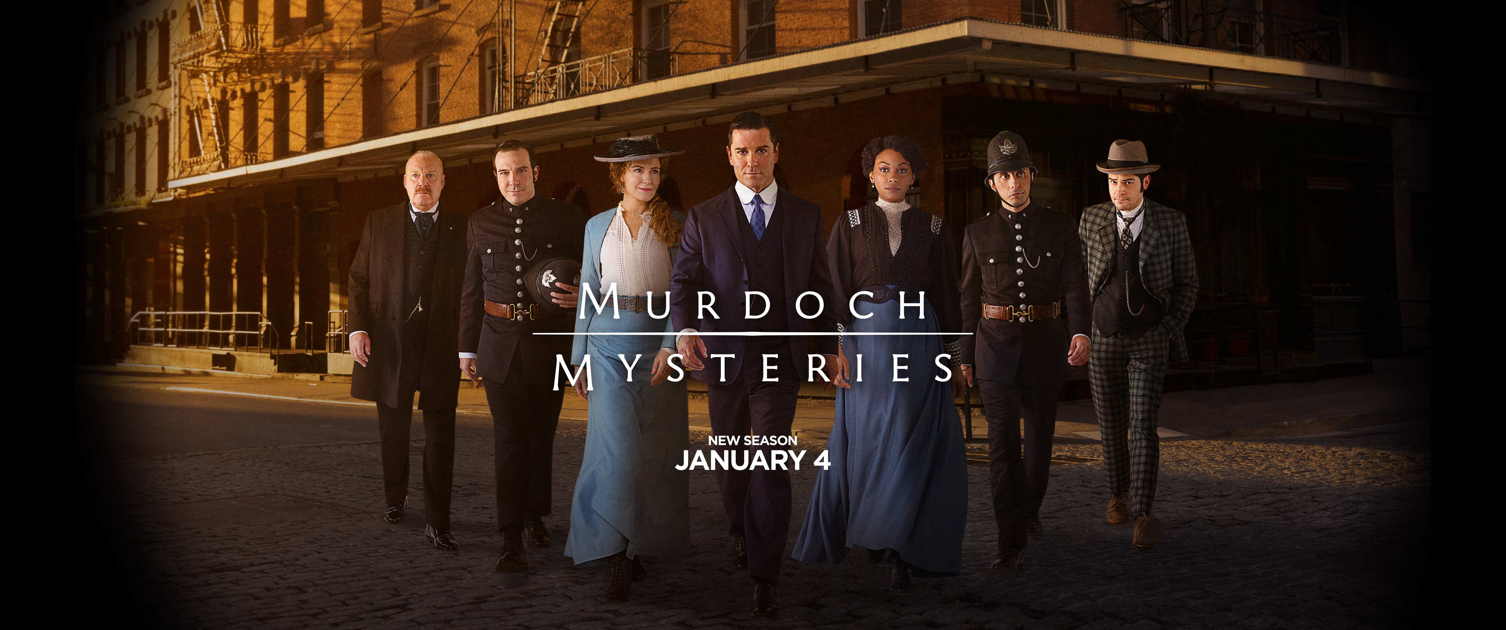 The cast of Murdoch Mysteries walk down a street at sunrise side by side, with Murdoch in the lead.